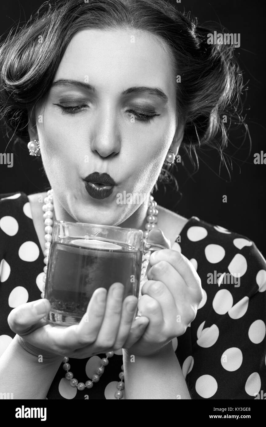 Pinup bella donna con la tazza di tè su sfondo nero guardando a soffiatura telecamera monocromatica Foto Stock
