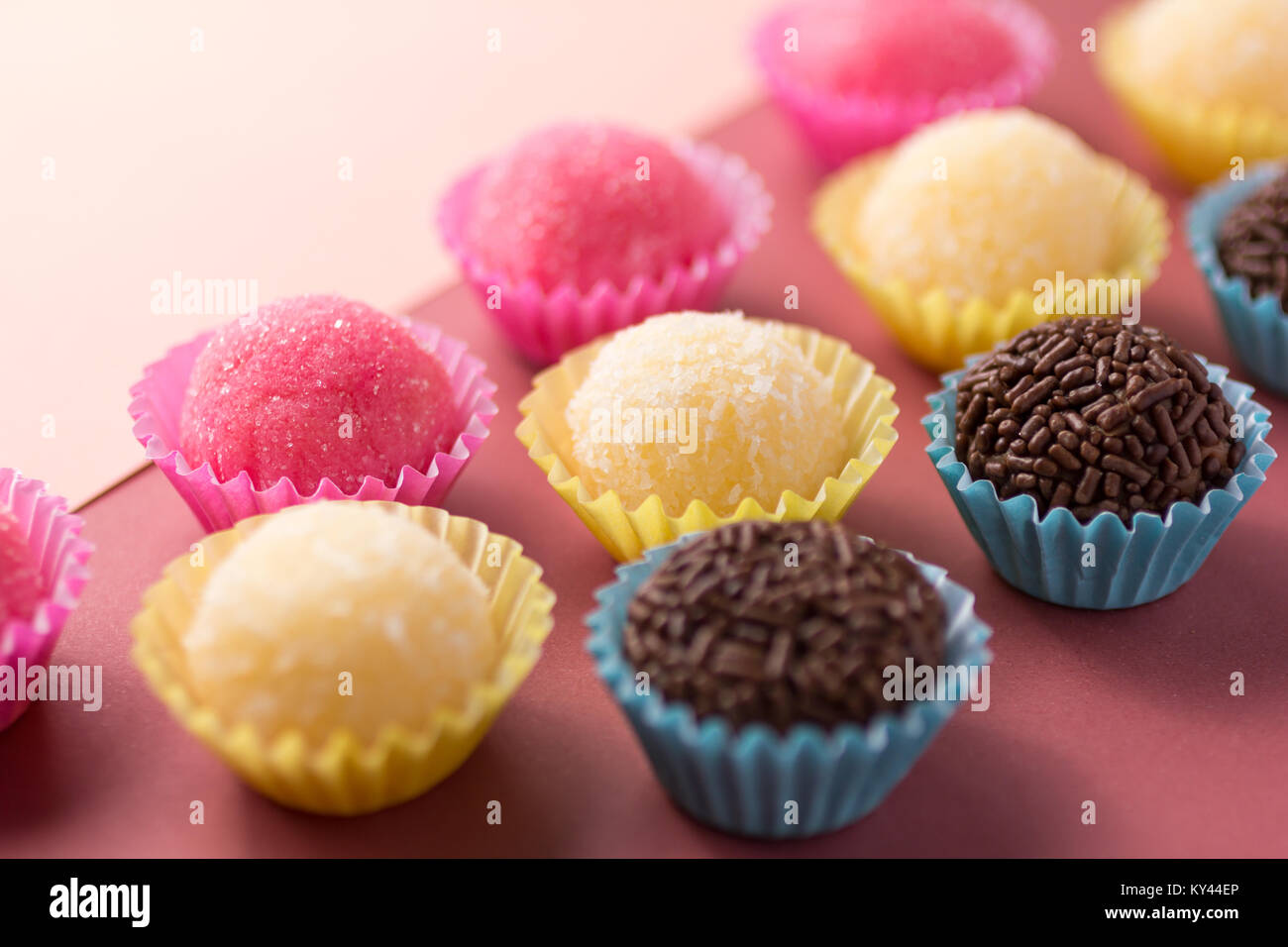 Caramelle brasiliano: Brigadeiro, Beijinho e Bicho de Pe. Bambini festa di compleanno. Le sfere di caramelle in una linea retta. Sfondo colorato. Foto Stock