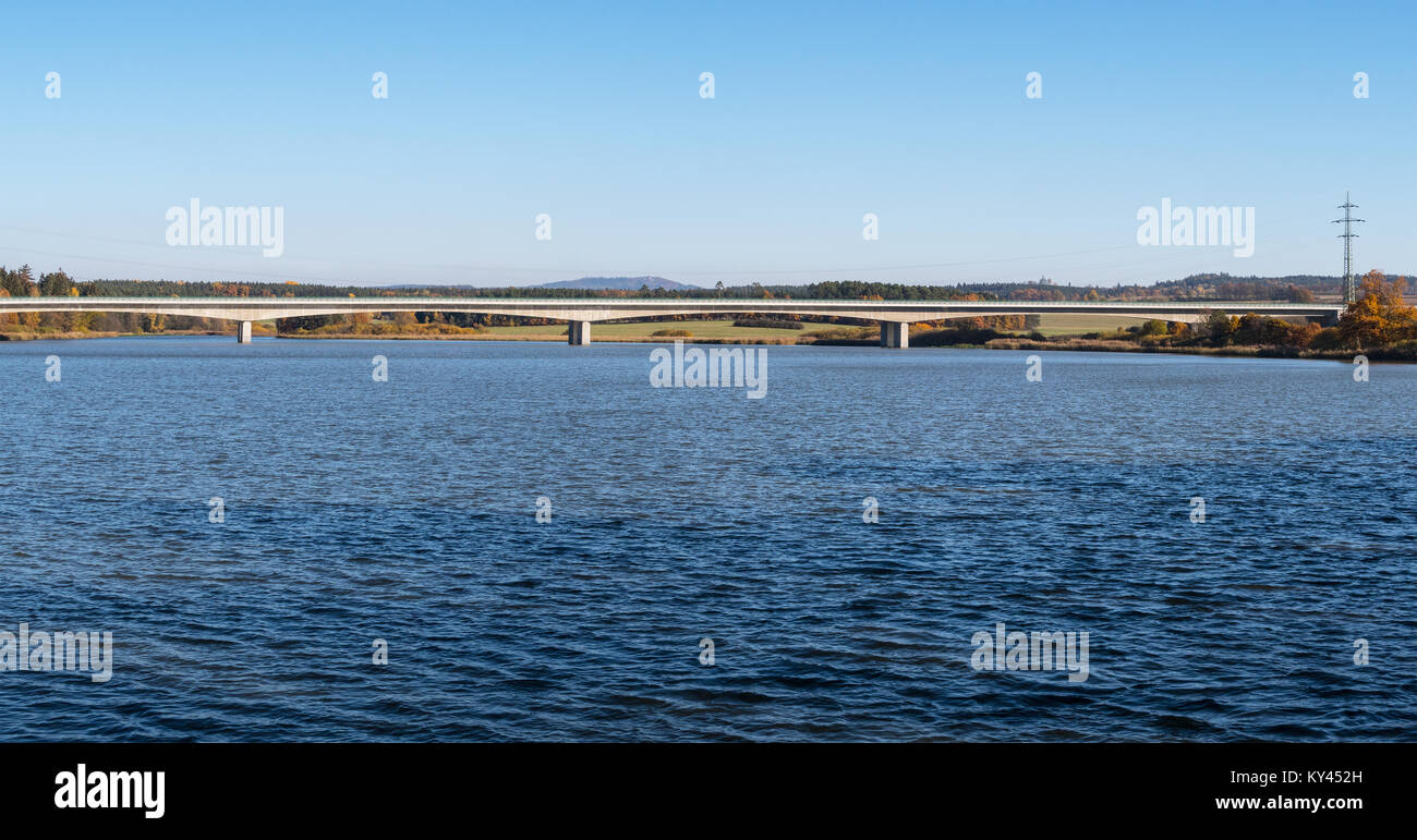 Bellissima vista del ponte autostradale in un'acqua. Paesaggio con stagno increspato in primo piano il ponte di cemento e una foresta all'orizzonte. Foto Stock