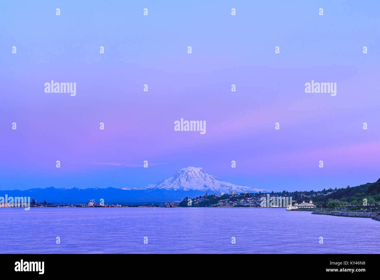 Mt Rainier sembra passare il puntatore del mouse sopra il centro cittadino di Tacoma come il sole di setting trasforma il cielo e la montagna sfumature di rosa e viola Foto Stock