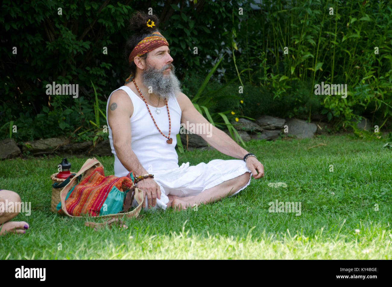 Uomo si siede con le gambe incrociate in erba guardando le prestazioni, Rhinebeck NY, STATI UNITI D'AMERICA Foto Stock