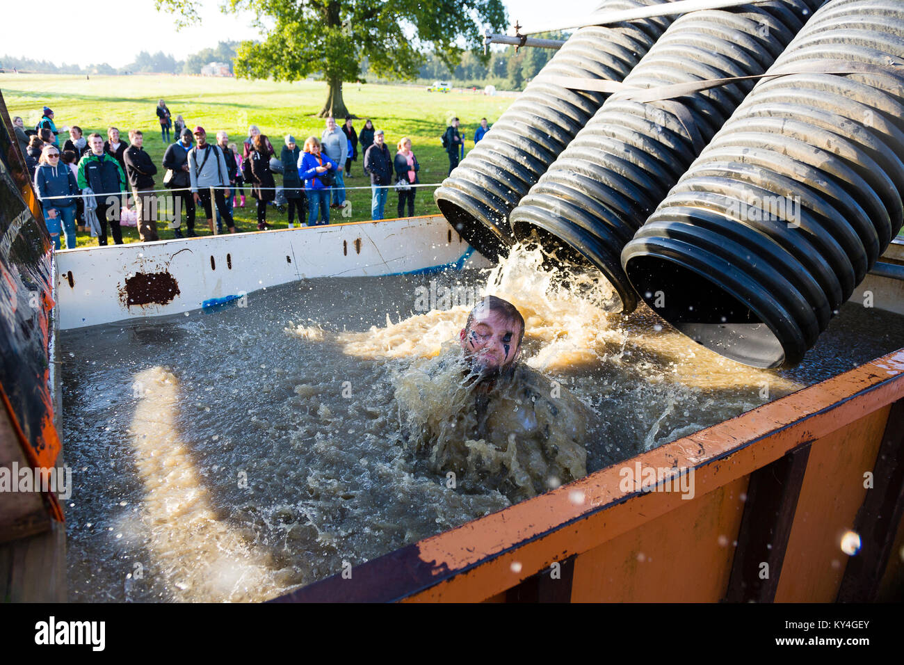 Sussex, Regno Unito. Un gruppo di spettatori guardare come un uomo scorre verso il basso un tubo di plastica nero in una grande piscina di acqua gelida durante una dura Mudder evento Foto Stock