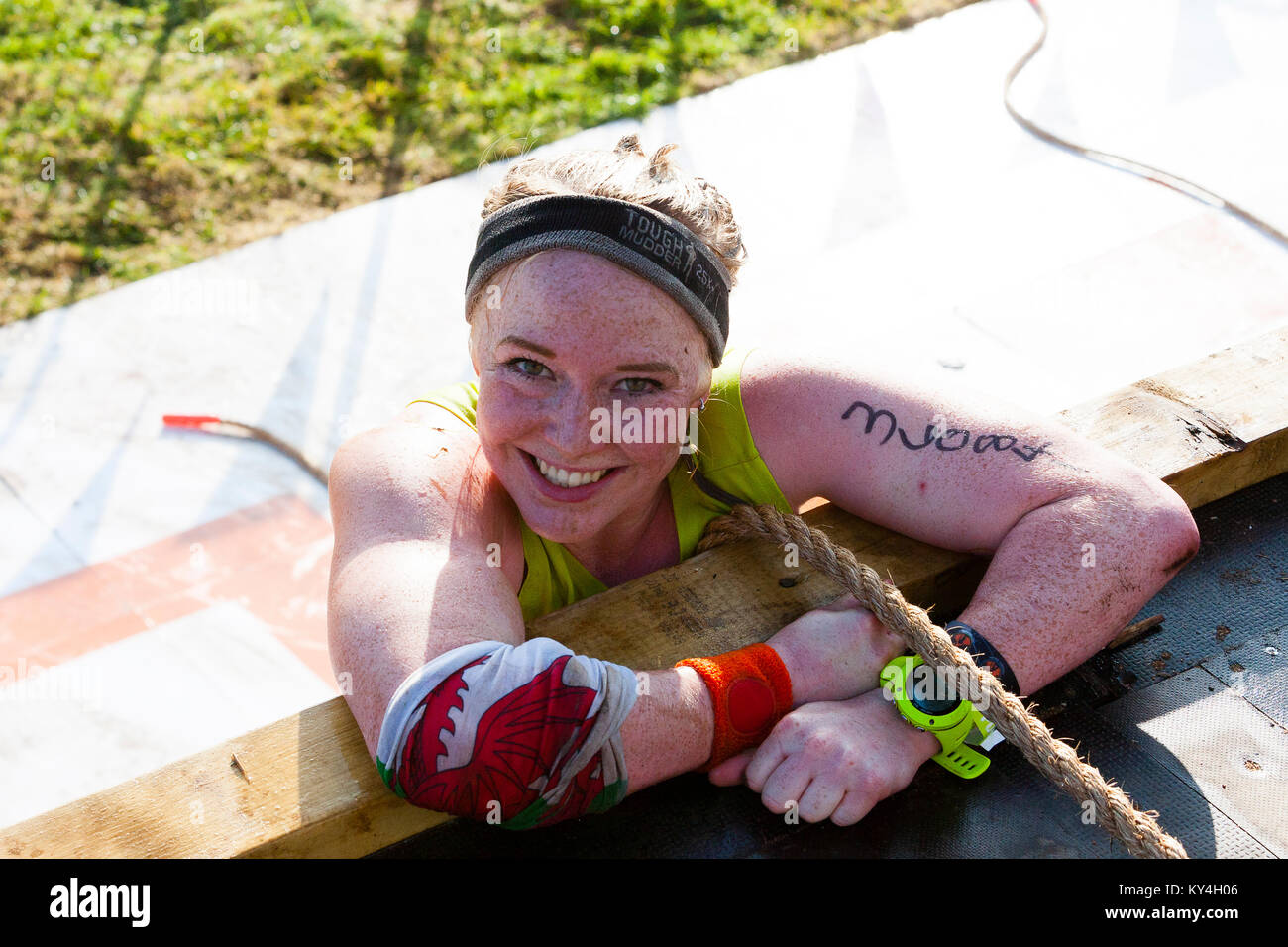 Sussex, Regno Unito. Una giovane donna sorrisi come lei si arrampica sopra la parte superiore dell'Everest 2.0 ostacolo durante una dura Mudder evento. Foto Stock