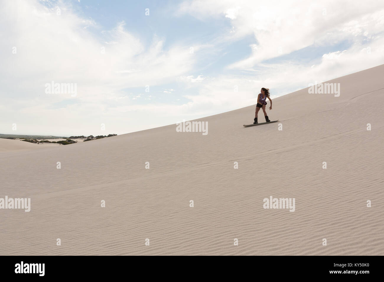 Sandboarding donna sulla duna di sabbia Foto Stock