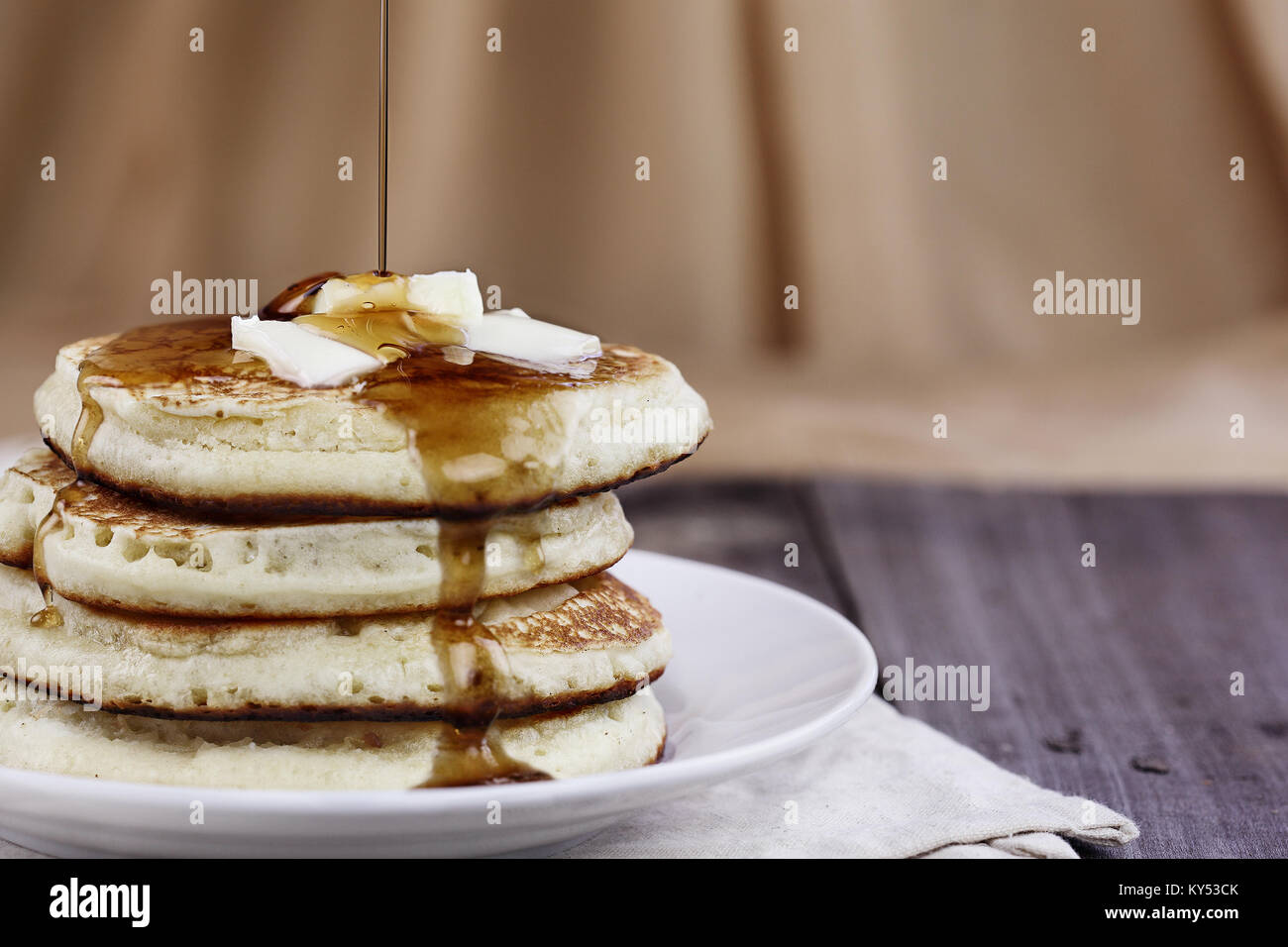 Pila di Pancake fatti in casa con burro di fusione e sciroppo essendo versata su di essi. Estrema profondità di campo. Perfetto per Martedì Grasso. Foto Stock