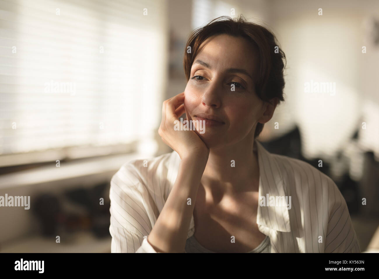 Giovane donna immissione mento sul lato che guarda lontano premurosamente a casa Foto Stock