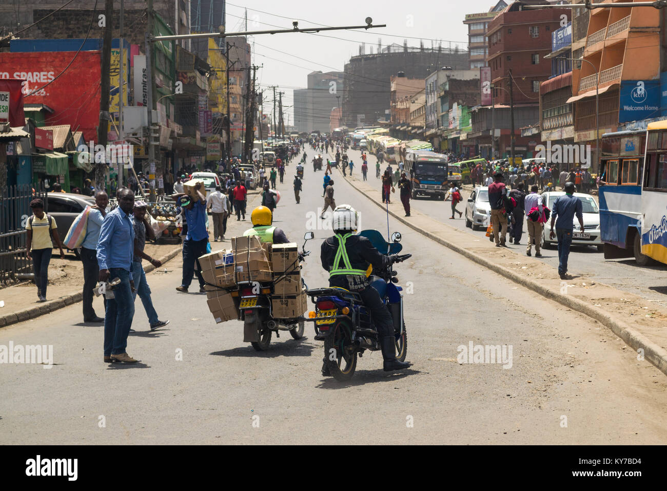 Moto auto giù per una lunga strada con edifici e persone su entrambi i lati, Nairobi, Kenya, Africa orientale Foto Stock