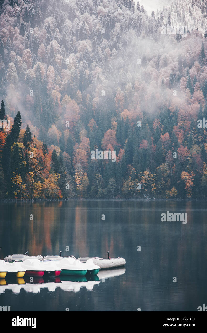 La nebbia di conifere in autunno la foresta e lago con barche sul paesaggio acqua concetto di viaggio sereno vista panoramica Foto Stock