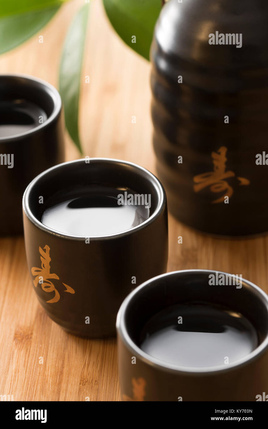 Sake Giapponese di vino di riso in bianco e nero e oro coppe con motivi bottiglia su un sfondo di bambù Foto Stock