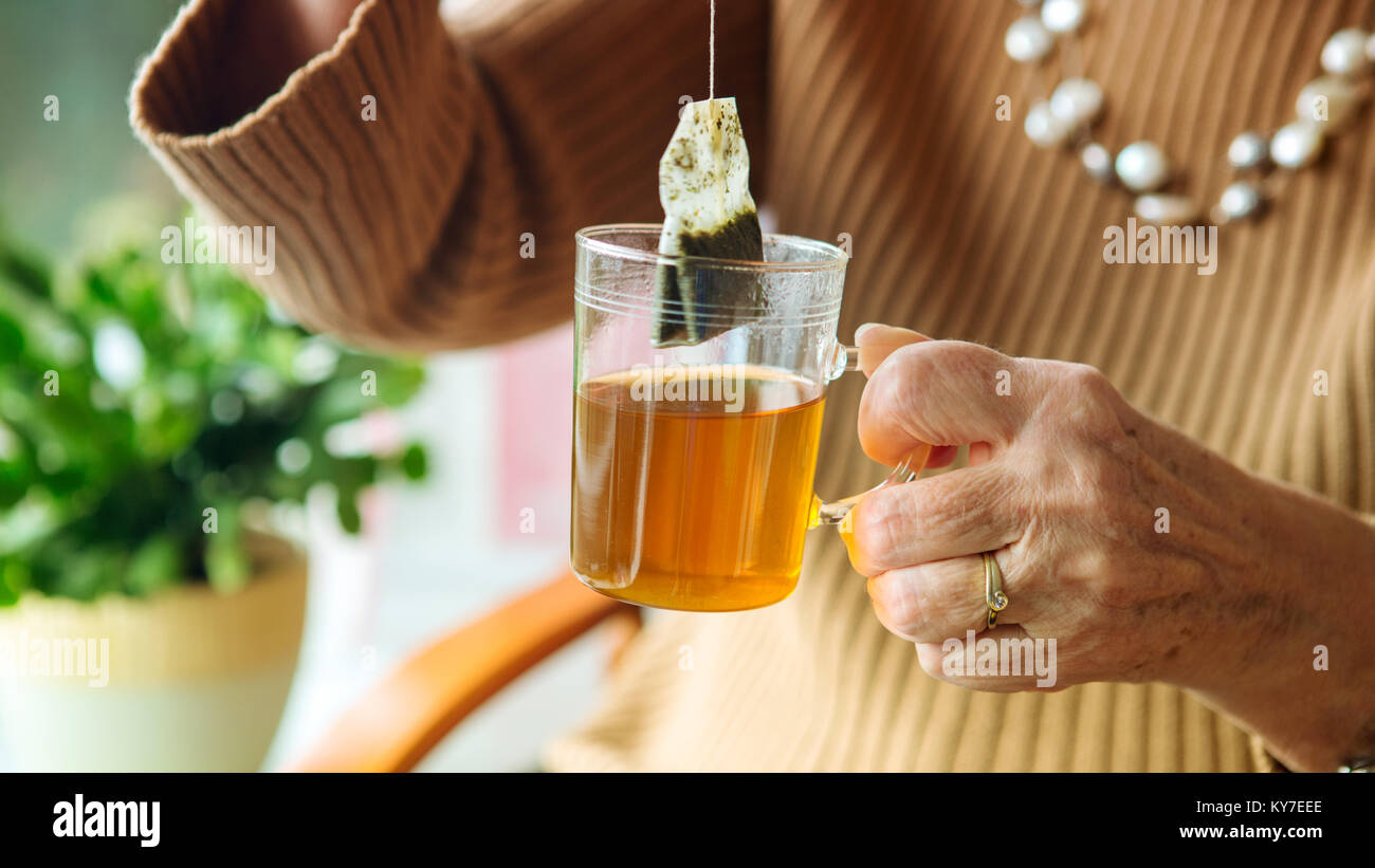 Donna anziana mano che tiene un bicchiere di tè con bustine di the Foto Stock