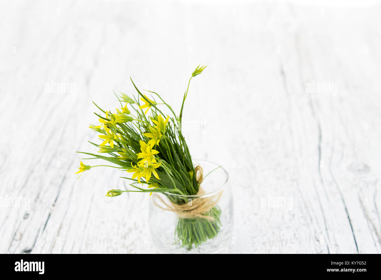 Bouquet di piccoli fiori gialli in un primo piano di vetro su un bianco sullo sfondo di legno Foto Stock