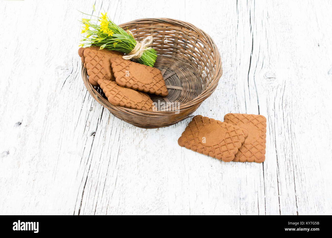 Piccolo bouquet di fiori gialli in un cesto di vimini con i cookie su un bianco sullo sfondo di legno Foto Stock