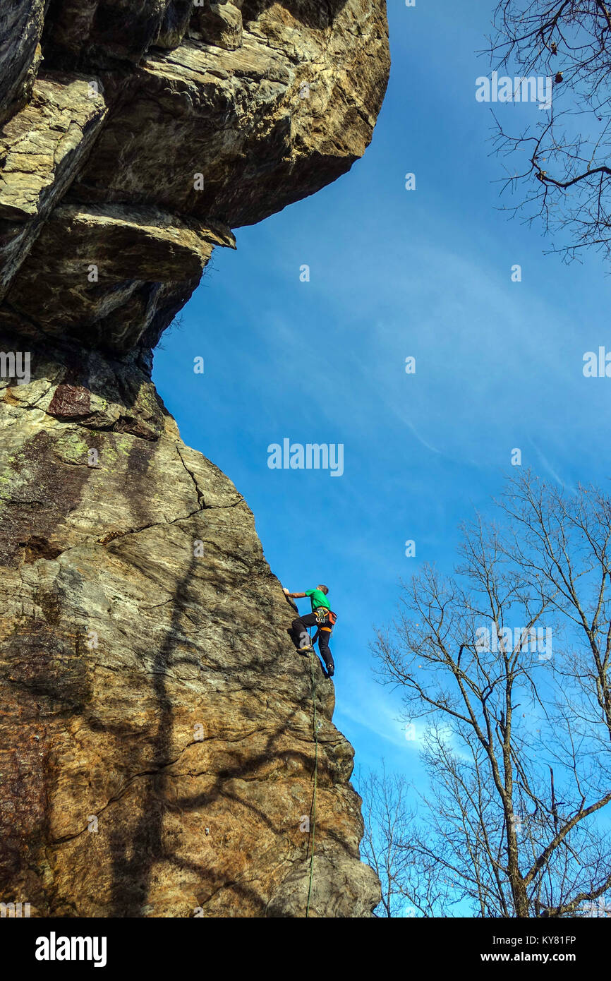 Maschio di rocciatore sulla ripida scogliera di granito con rocce rosse e blu cielo Foto Stock