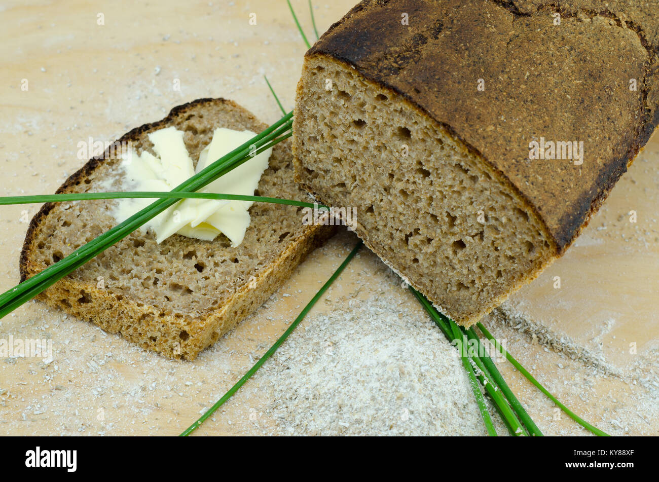 Fresco di pane di segale imburrato con slice e chieves su un tagliere di legno Foto Stock