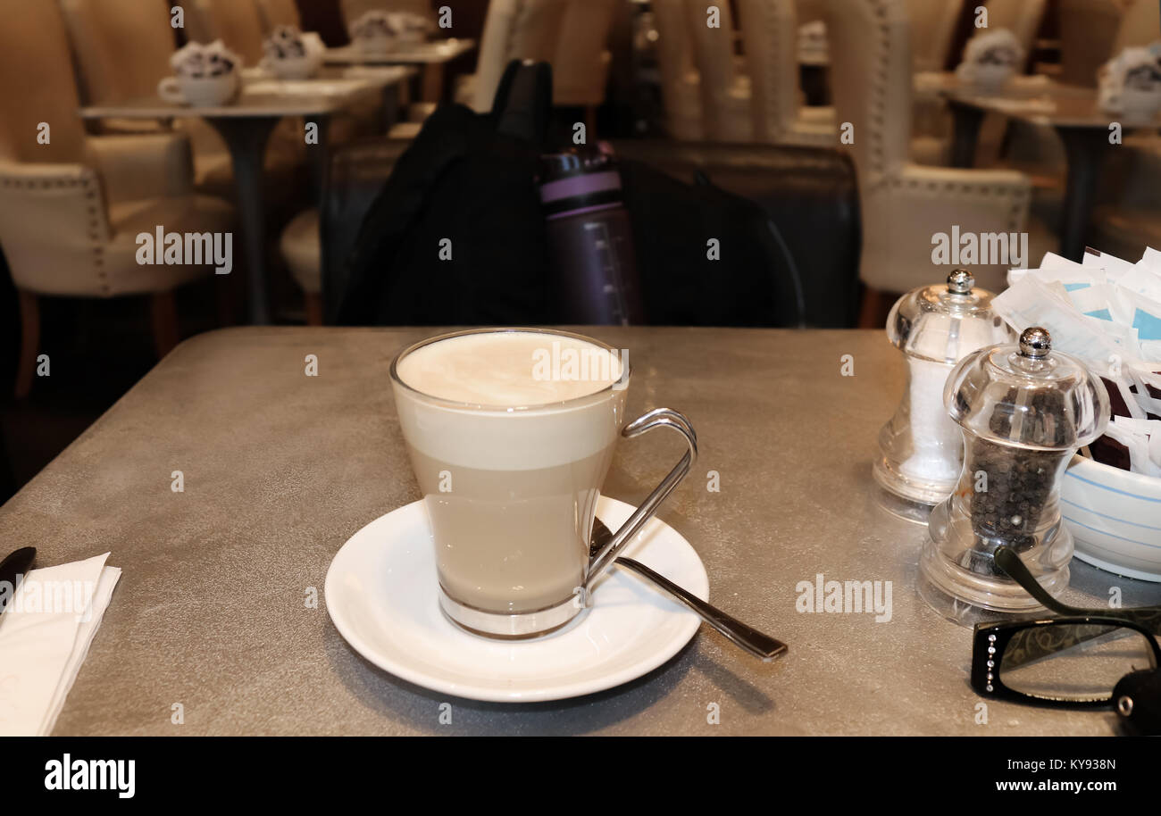 Viaggiare da soli - tazza di latte su un tavolo in un aeroporto con uno zaino e una bottiglia d'acqua in cattedra e sedie e tavoli in sfondo.jpg Foto Stock