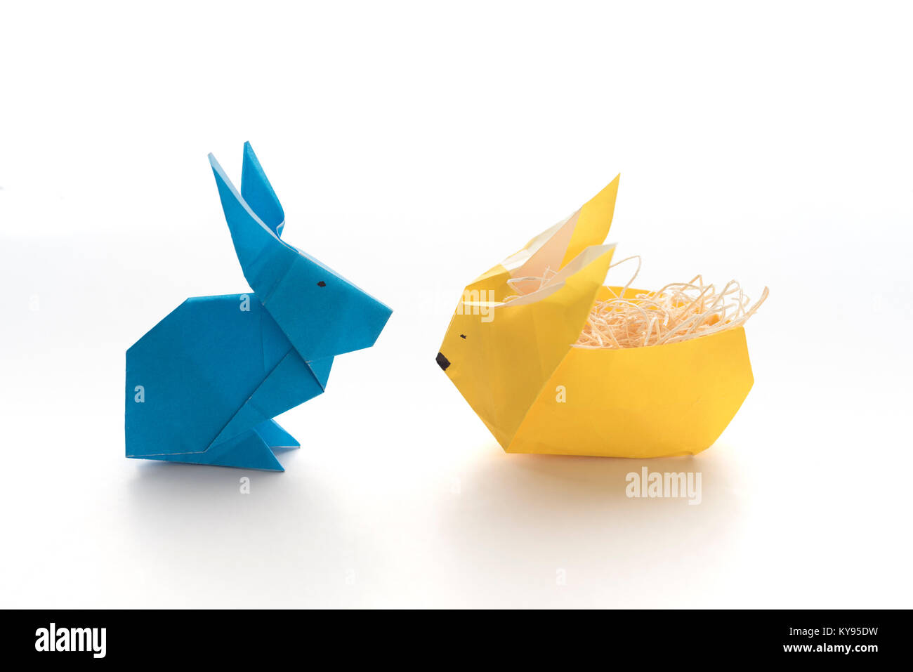 Due coloratissimi origami conigliette fatta di carta in giallo e blu, uno farcito con paglia, pronto per le uova di Pasqua, isolati su sfondo bianco Foto Stock