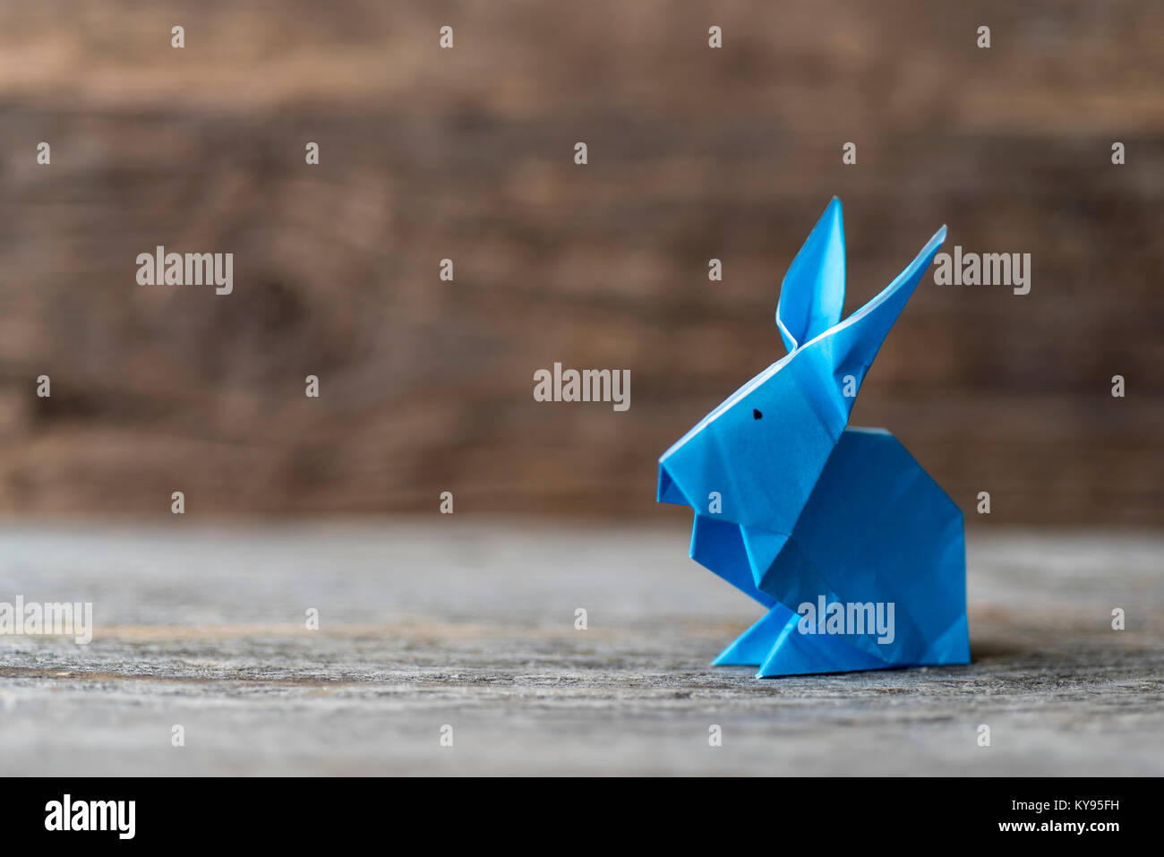 Colorato origami Easter Bunny rabbit realizzato in carta blu, pronto per la Pasqua o primavera, contro rustico in legno marrone sfondo Foto Stock