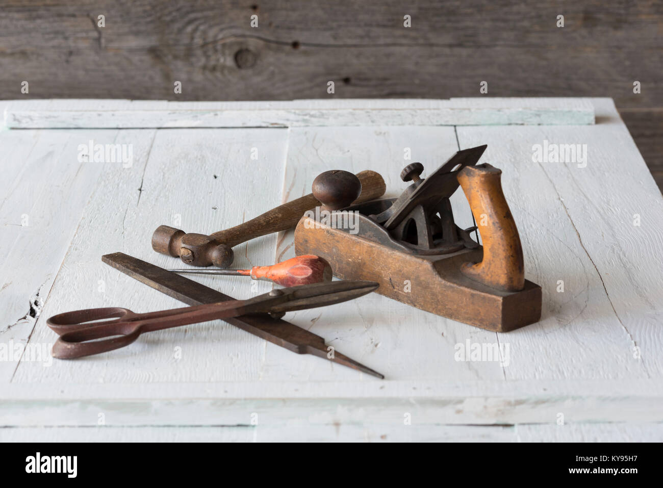 Collezione di antichi, weathered strumenti vintage, compreso il martello, AWL, file tin snips e blocco di legno piano, contro weathered verniciato bianco ba in legno Foto Stock