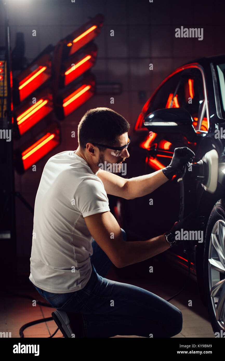 Dettagli auto - uomo con lucidatrice orbitale nel negozio di riparazioni auto. Messa a fuoco selettiva. Foto Stock