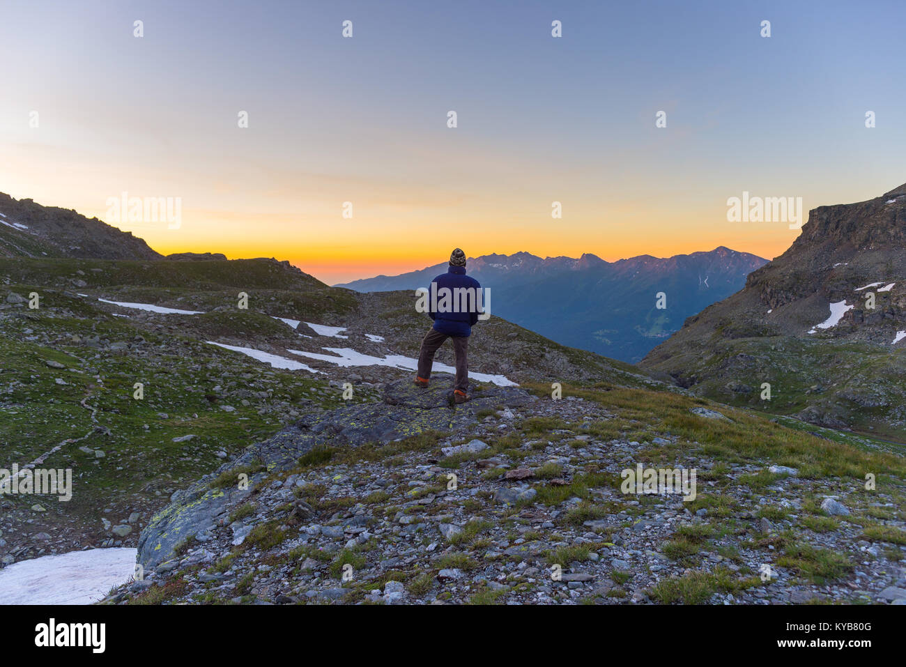Una persona che guarda alba colorata in alto nelle Alpi. Ampio angolo di visione da sopra con incandescente picchi di montagna in background. Avventura estate Foto Stock