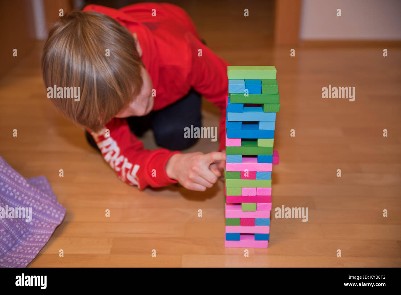 Ragazzo con attenzione il prelievo di un componente di un colorato Jenga aka Klodsmajor gioco sociale in cui costruire una torre di pezzi di legno fino a che non collassa uns Foto Stock