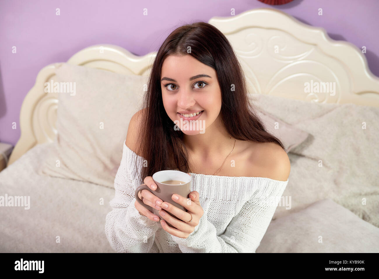 La bruna ragazza nel letto con una tazza. Giovane donna sorridente guardando la telecamera, tenendo la tazza con il caffè. Foto Stock