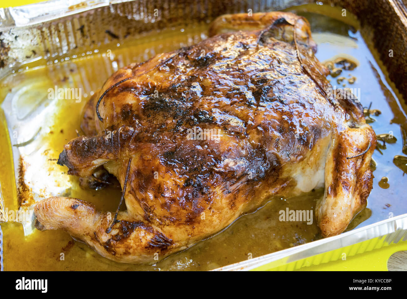 Spiedo di pollo arrosto con i suoi grassi in un contenitore metallico Foto Stock