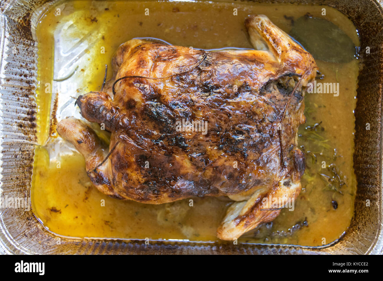 Spiedo di pollo arrosto con i suoi grassi in un contenitore metallico Foto Stock