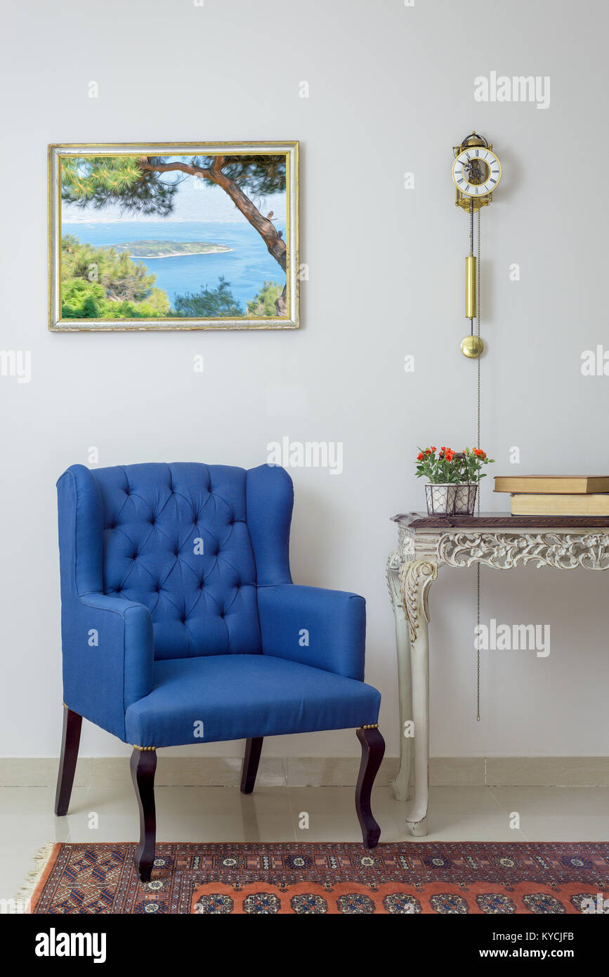 Mobili Vintage - composizione interna di retro blu poltrona, vintage in legno tavolo beige e orologio a pendolo su off parete bianca, con piastrelle pavimento beige Foto Stock