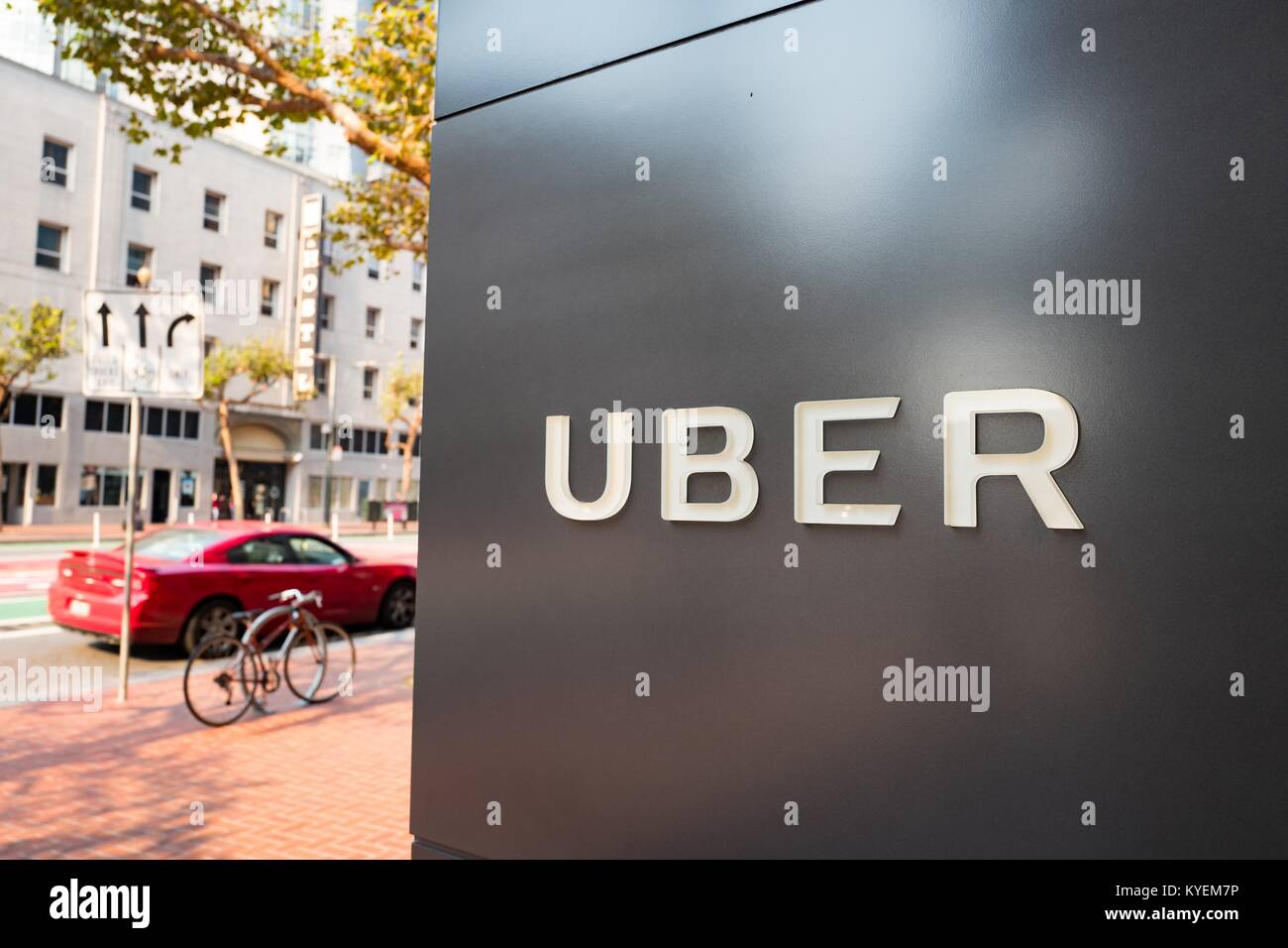 Cartello con il logo presso la sede centrale di car-sharing technology company Uber nel sud del mercato (SOMA) quartiere di San Francisco, California, con il rosso veicolo visibile in background parcheggiato su Market Street, 13 ottobre 2017. SoMa è noto per avere una delle più alte concentrazioni di aziende di tecnologia e di startup di qualsiasi altra regione del mondo. () Foto Stock