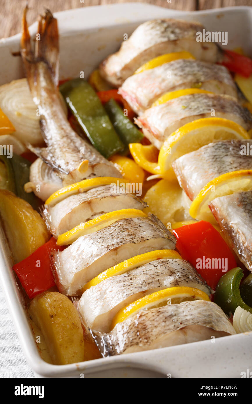 Merluzzo bianco intero cotto con verdure e limone in una teglia da forno da vicino sul piano verticale. Foto Stock