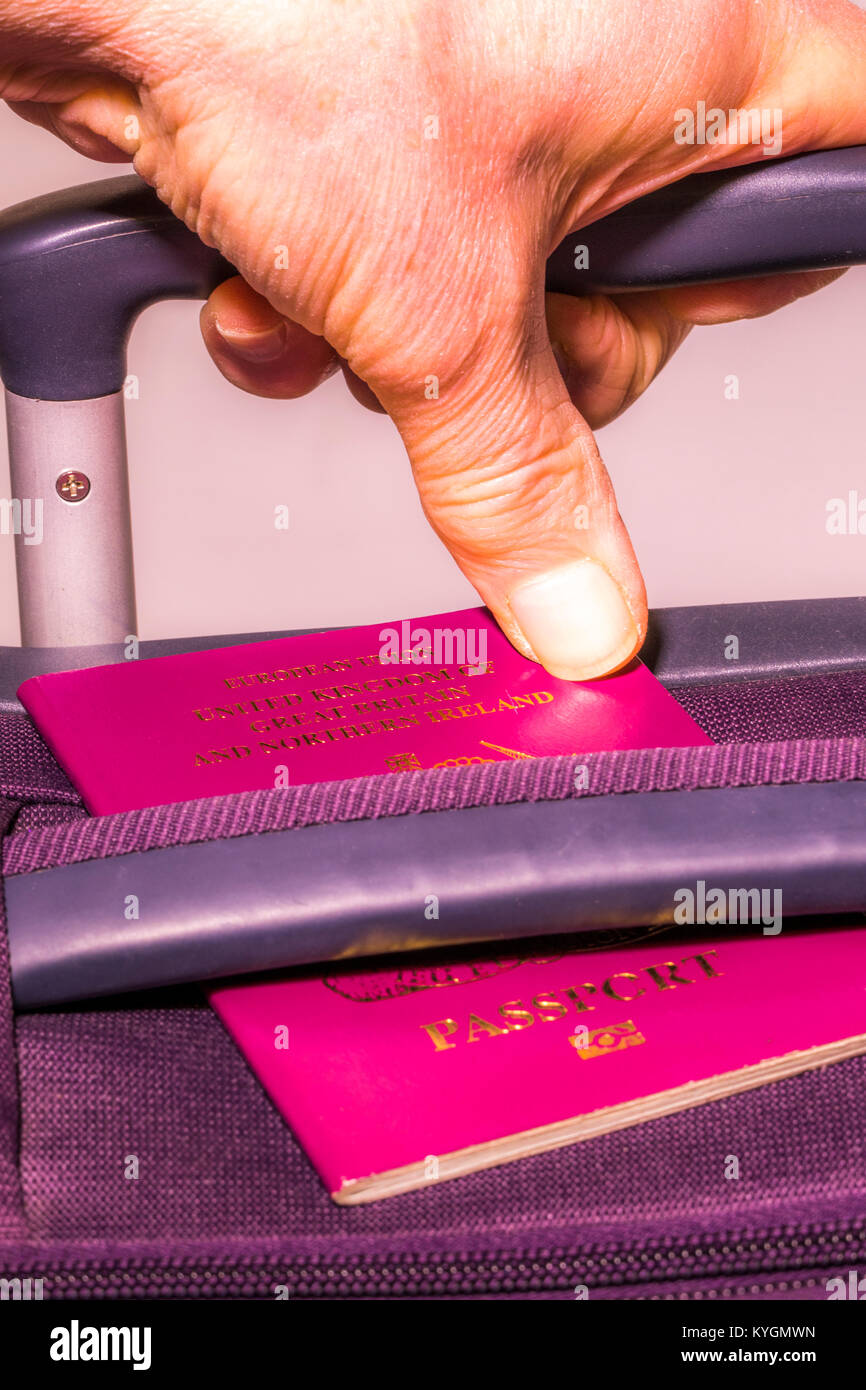 Mano d'uomo in possesso di una maniglia di valigia con un pollice che fissano un passaporto del Regno Unito mostra: Unione Europea Regno Unito di Gran Bretagna e Irlanda del Nord. Foto Stock