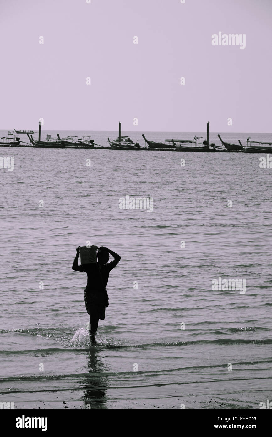 Il lavoro manuale. Lo scarico di merci da un tradizionale longtail boat a Railay Beach, Krabi Provence, Thailandia Foto Stock