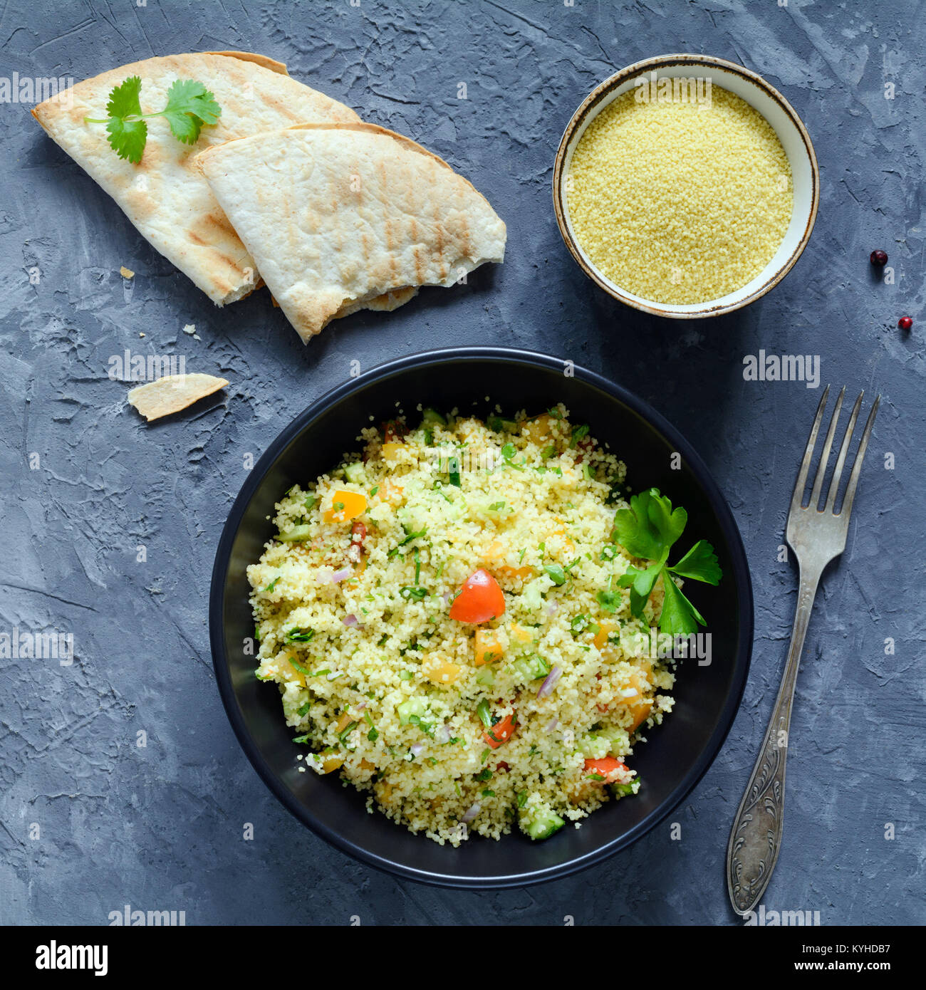 Tabulé insalata e flatbread su sfondo di calcestruzzo. Libanese, cucina araba. Vegano sano cous cous insalata in ciotola nero. Tabella vista superiore, quadrato cr Foto Stock