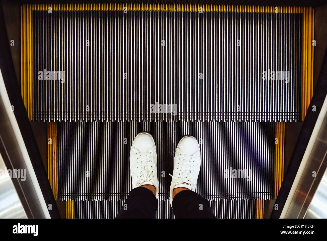 Selfie dell uomo in piedi in bianco scarpe sneaker sulle fasi di escalator nel centro commerciale per lo shopping, vista dall'alto in stile vintage Foto Stock