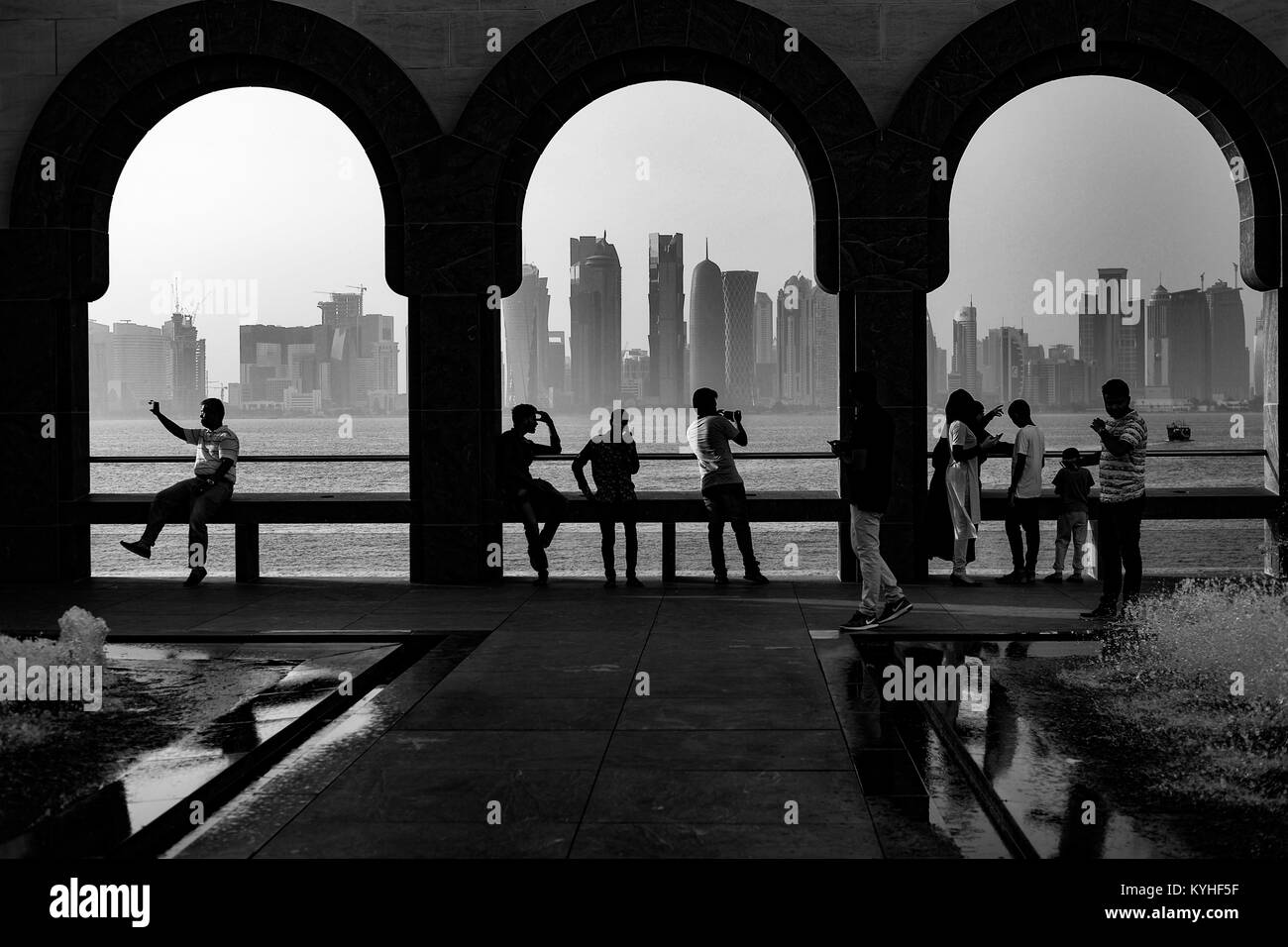 La skyline di Doha appare attraverso le arcate del Museo di Arte Islamica. La gente, in forma di silhouette, sedersi sulla mensola a prendere in Qatar la capitale. Foto Stock