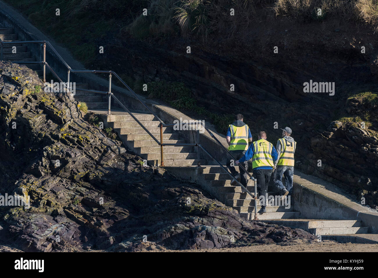 Tre lavoratori edili indossa hi-viz giacche salendo passaggi su Polzeath Beach a nord della costa della Cornovaglia. Foto Stock
