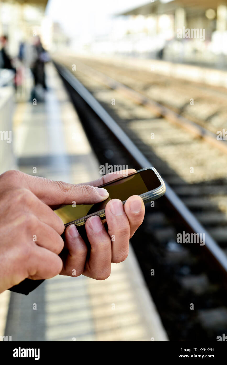 Primo piano di un giovane uomo caucasico utilizzando uno smartphone in un esterno in treno o in stazione dei tram Foto Stock