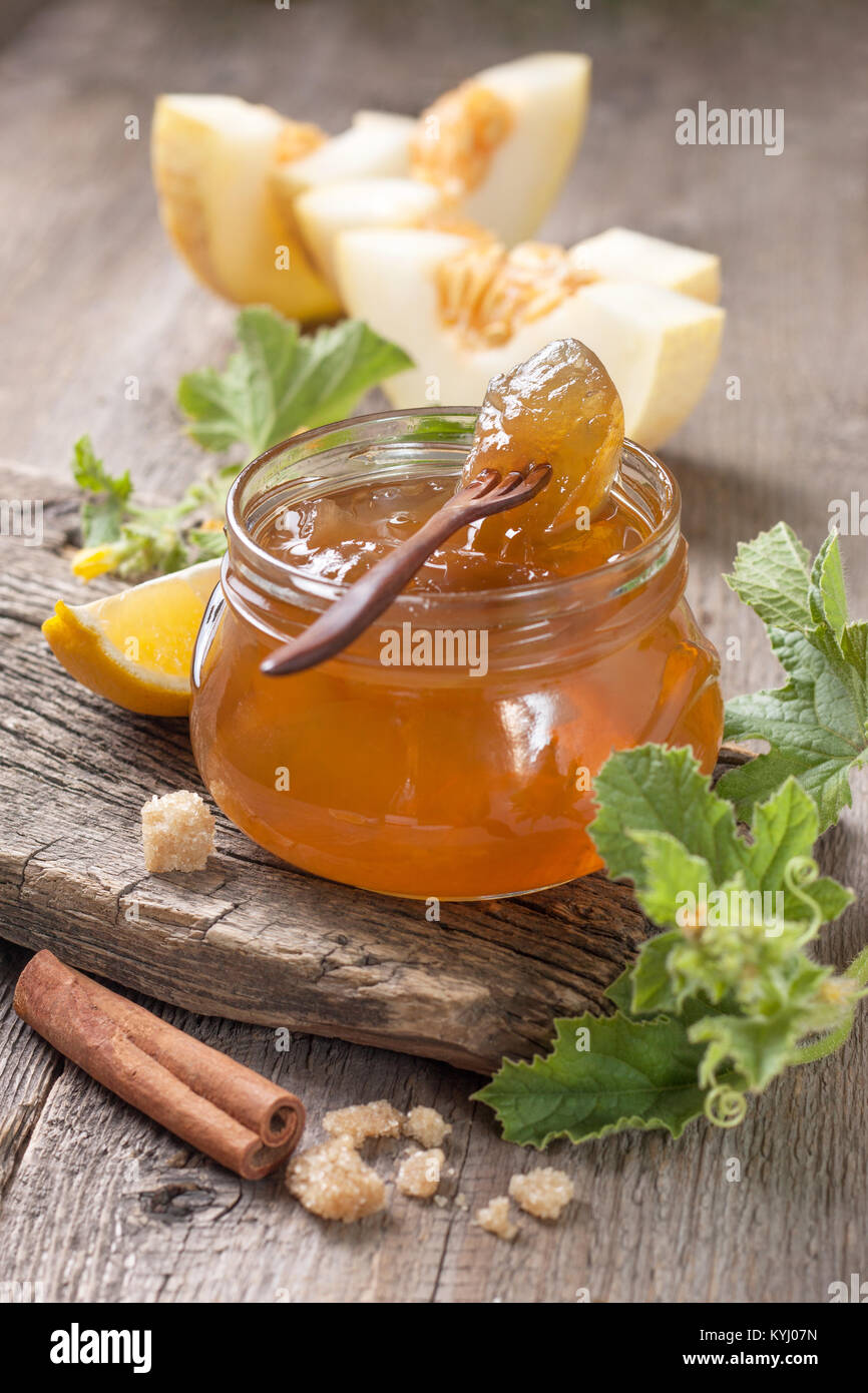 Melone marmellata in un barattolo di vetro, fette di melone su uno sfondo di legno Foto Stock