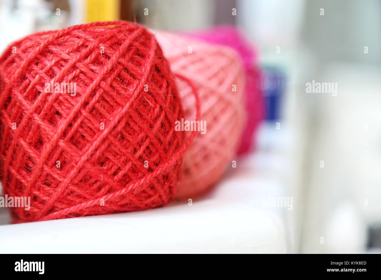 Colorate filato per maglieria di sfere e aghi sul tavolo bianco contro sfondo sfocato. Close up multi colore palle di lana. Foto Stock