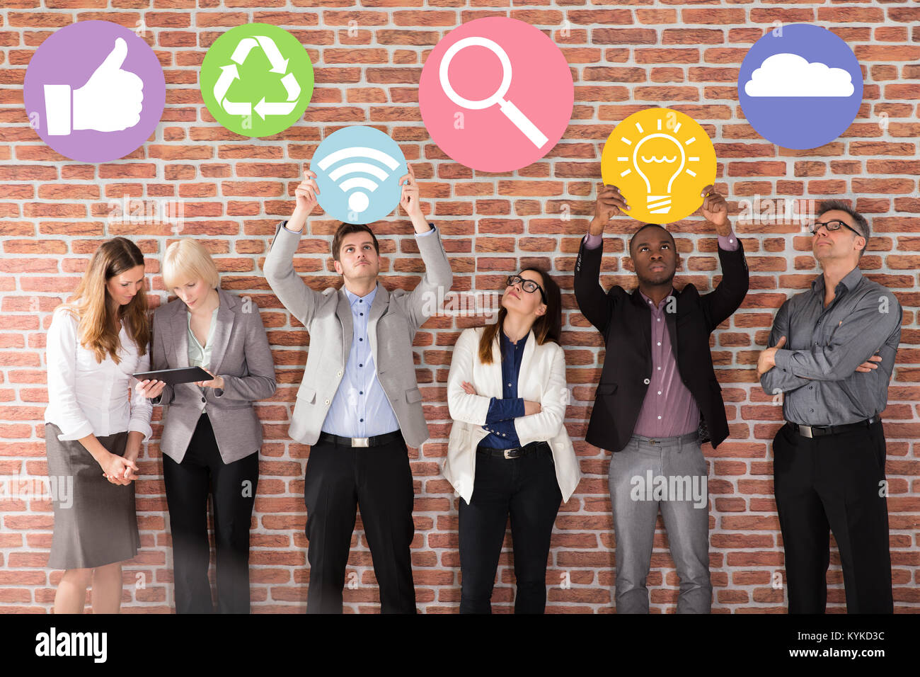 Diversi imprenditori in piedi vicino al muro di mattoni Holding Simboli aziendali Foto Stock