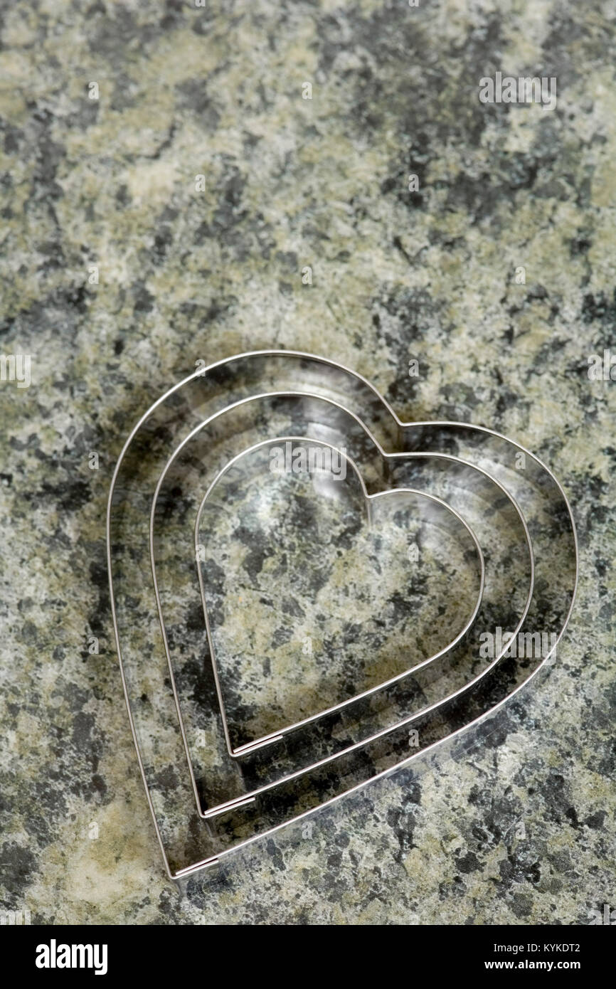 Un set di tre a forma di cuore ad cookie cutters su un effetto marmo piano della cucina Foto Stock