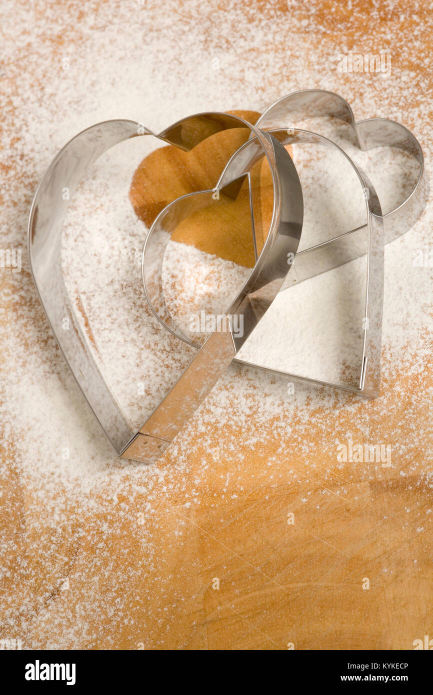 Un set di tre a forma di cuore ad cookie cutters su una spolverata di farina di sfondo Foto Stock