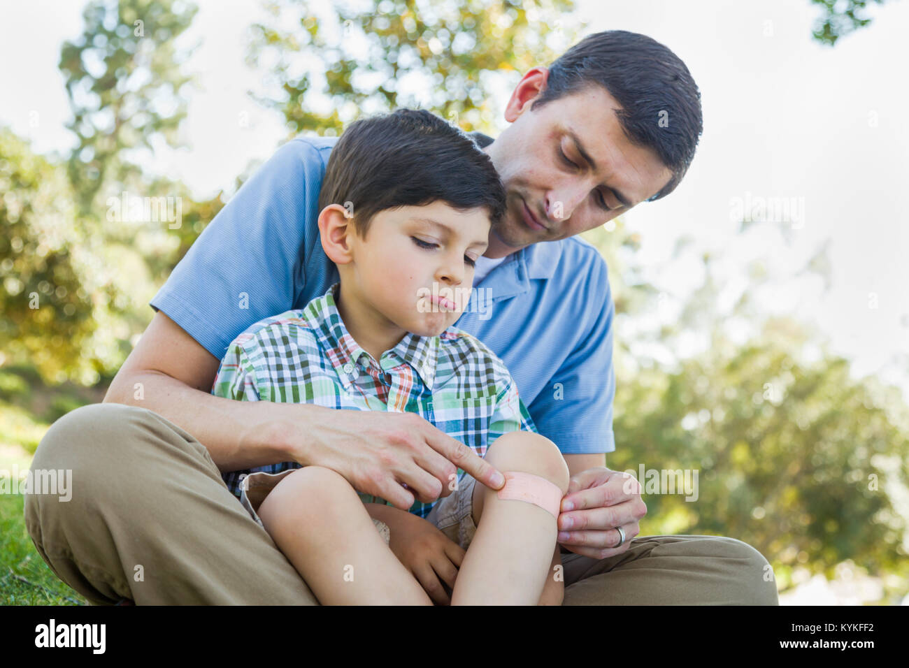 Padre amorevole mette una benda sul gomito del suo giovane figlio nel parco. Foto Stock