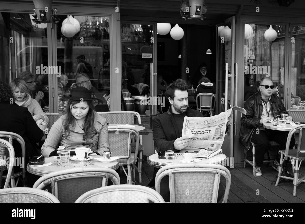 Parigi-Jan 2, 2014: Persone aventi il caffè, la lettura della carta in un locale tipico Sidewalk Cafe, che può essere visto in tutta Parigi. In bianco e nero foto Foto Stock