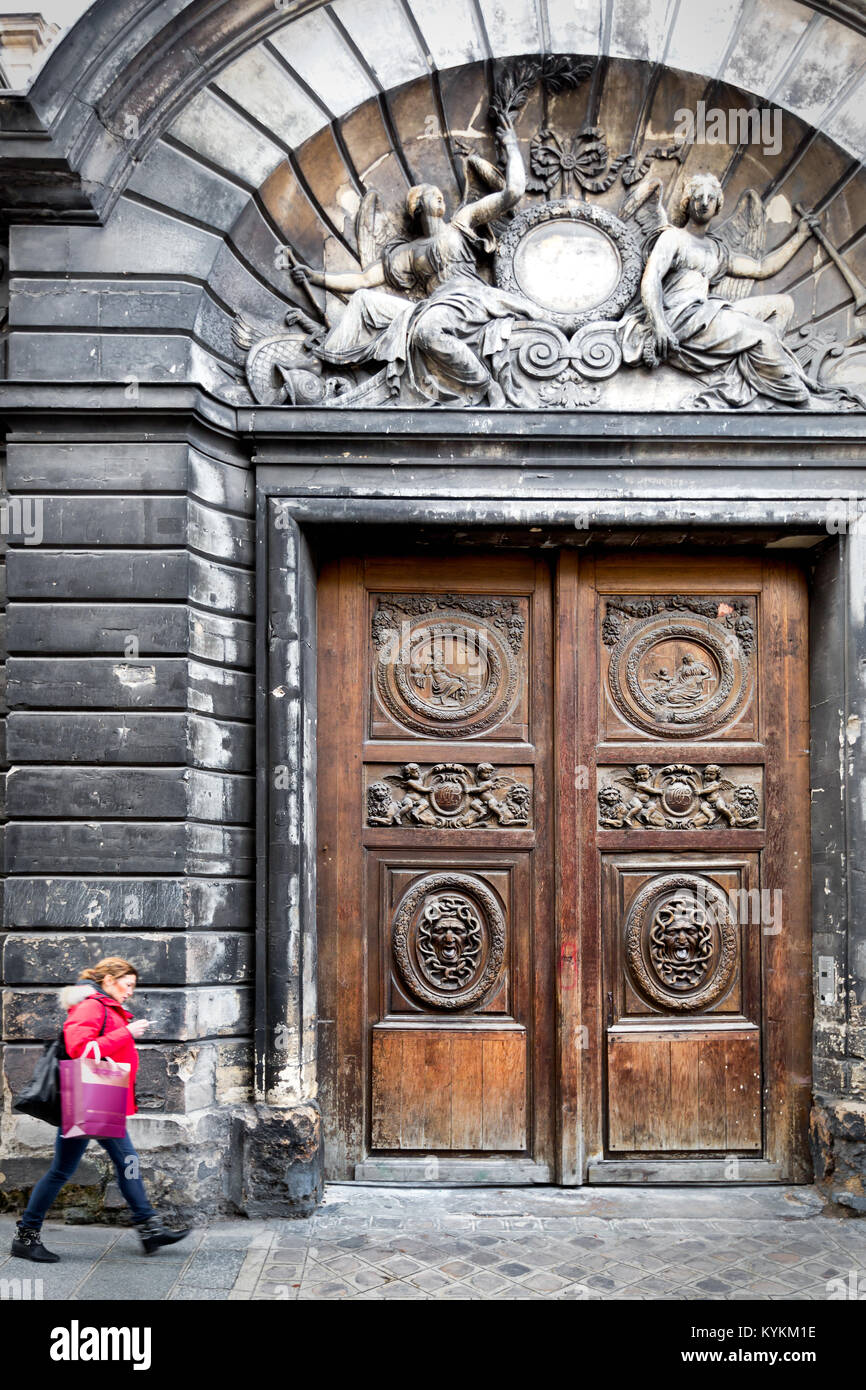 Parigi enorme vecchio scolpiti ornano esterno porte in legno. Marais Quartiere storico. Donna cammina guardando il suo telefono. Foto Stock