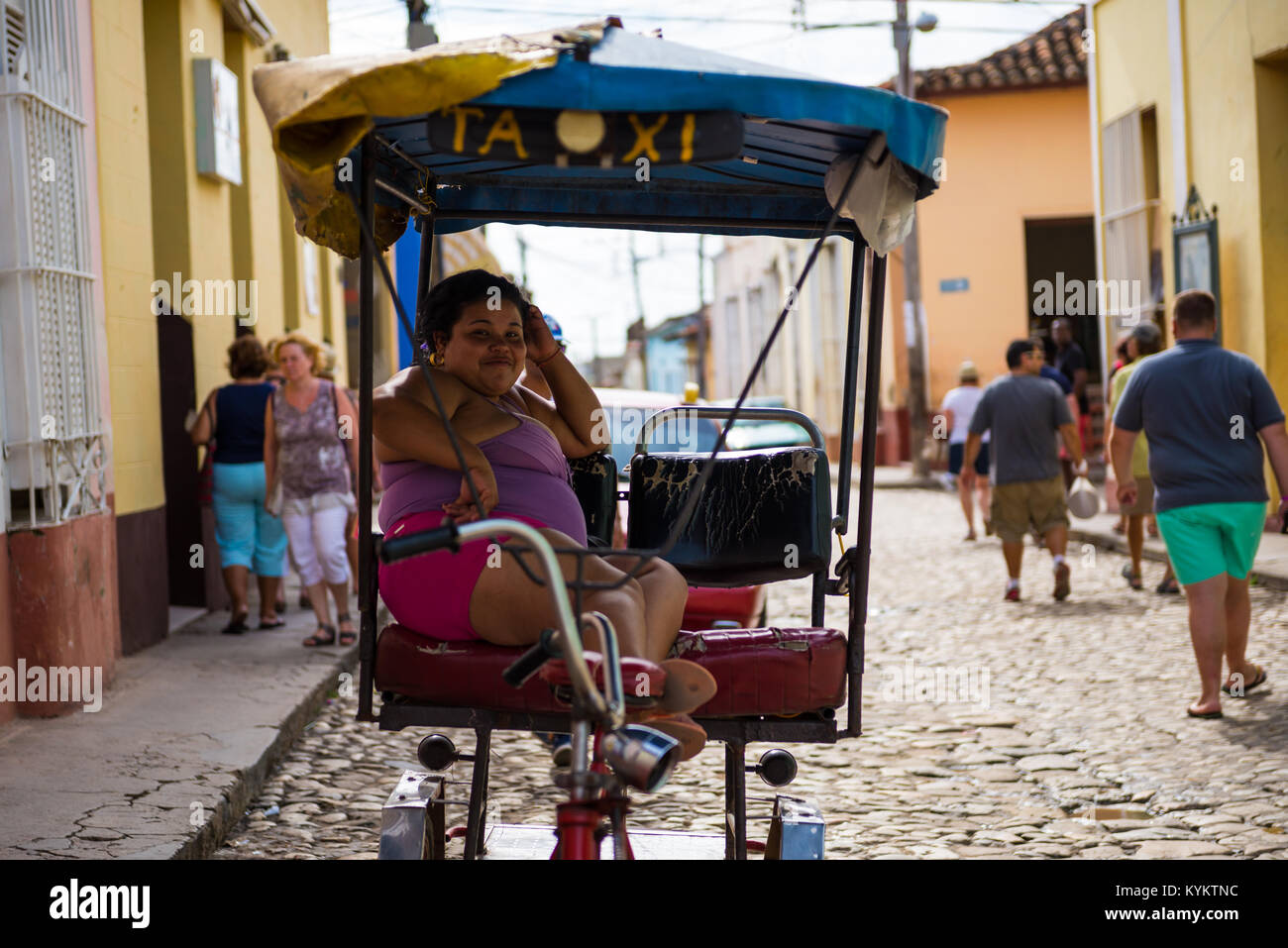 Trinidad, Cuba - 26 Novembre 2015: un sorridente donna cubana si siede in un pedale bike taxi mentre le persone stanno camminando per le strade dietro di lei Foto Stock