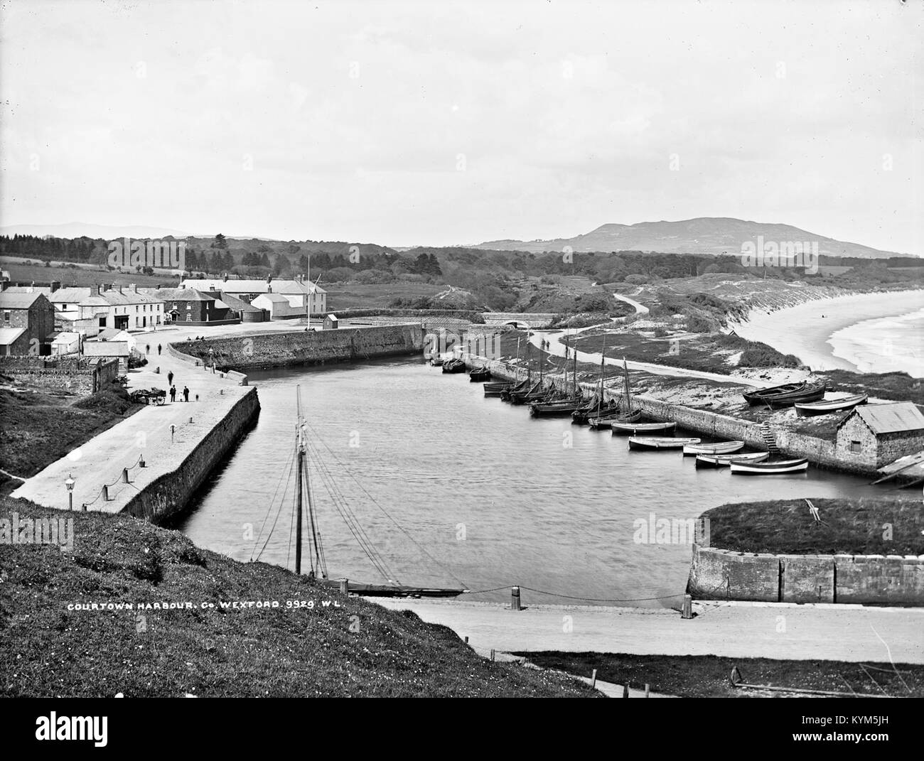 Un bicchiere negativo di Courtown Harbour, Co. Wexford, che cattura la bellezza panoramica del porto, delle barche e della spiaggia circostante. La foto, parte della Lawrence Collection, offre uno sguardo storico sulla vita costiera irlandese. Foto Stock