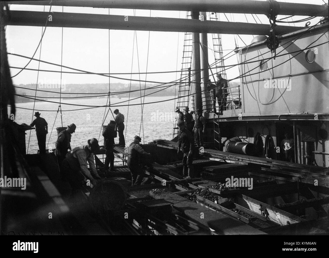 Una fotografia storica che mostra i lavoratori che caricano cesti di carbone su una nave, catturando l'attività industriale del tempo e la logistica coinvolta nel commercio del carbone. L'immagine riflette i metodi di manodopera e trasporto utilizzati durante questo periodo. Foto Stock