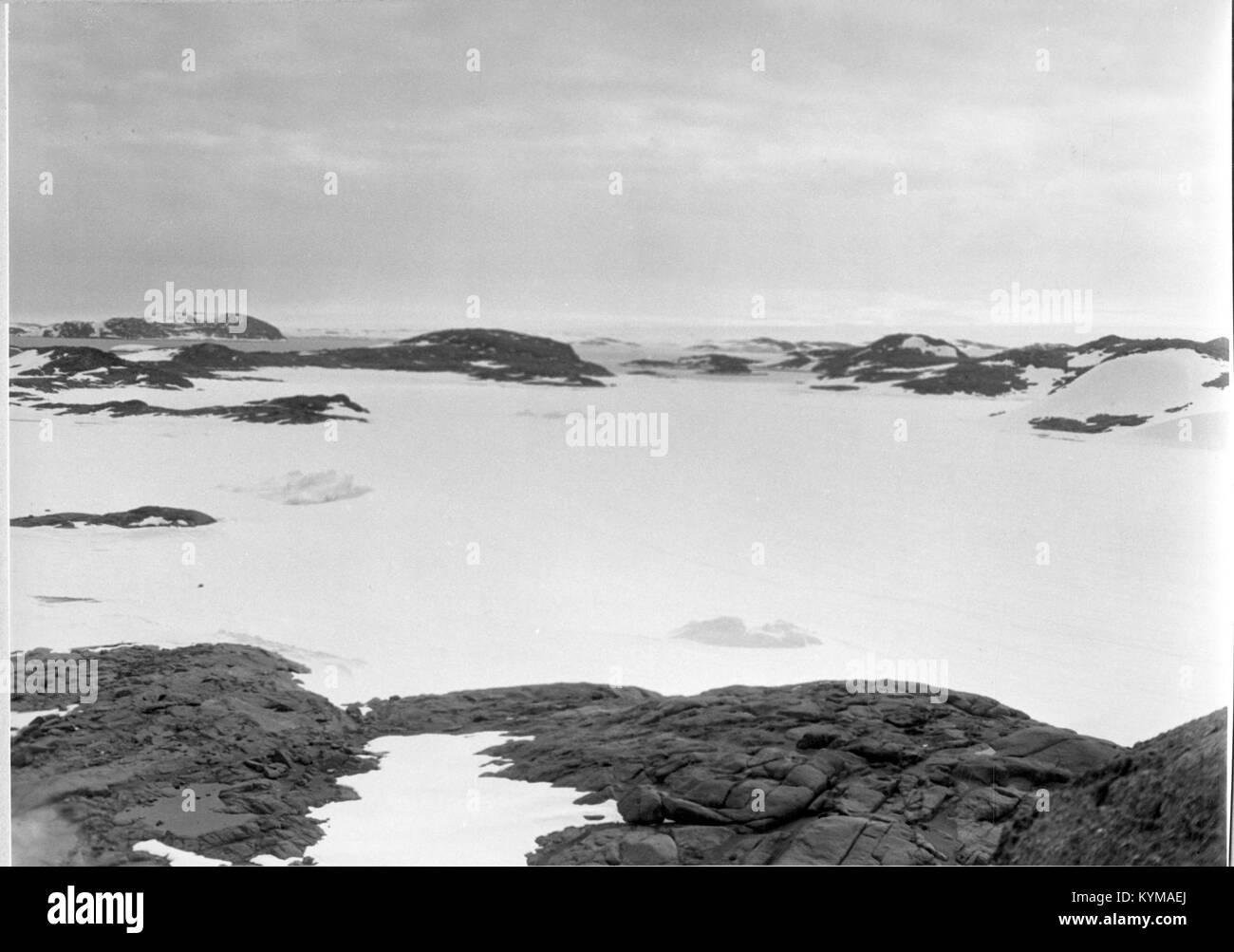 Una fotografia aerea dell'Antartide, caratterizzata da un paesaggio aspro con rocce scure in contrasto con il terreno ghiacciato. L'immagine cattura la topografia unica e aspra del continente, scattata durante l'operazione Windmill. Foto Stock